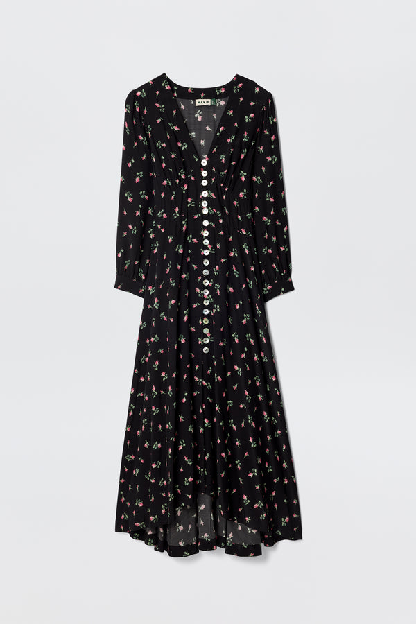 The Avalyn - Sienna Bud Black is a long-sleeved, black silk tea dress with a V-neckline, white buttons, vintage-style cuffs, and a pink and green floral print. Its loose, flowy silhouette offers an elegant, timeless look.