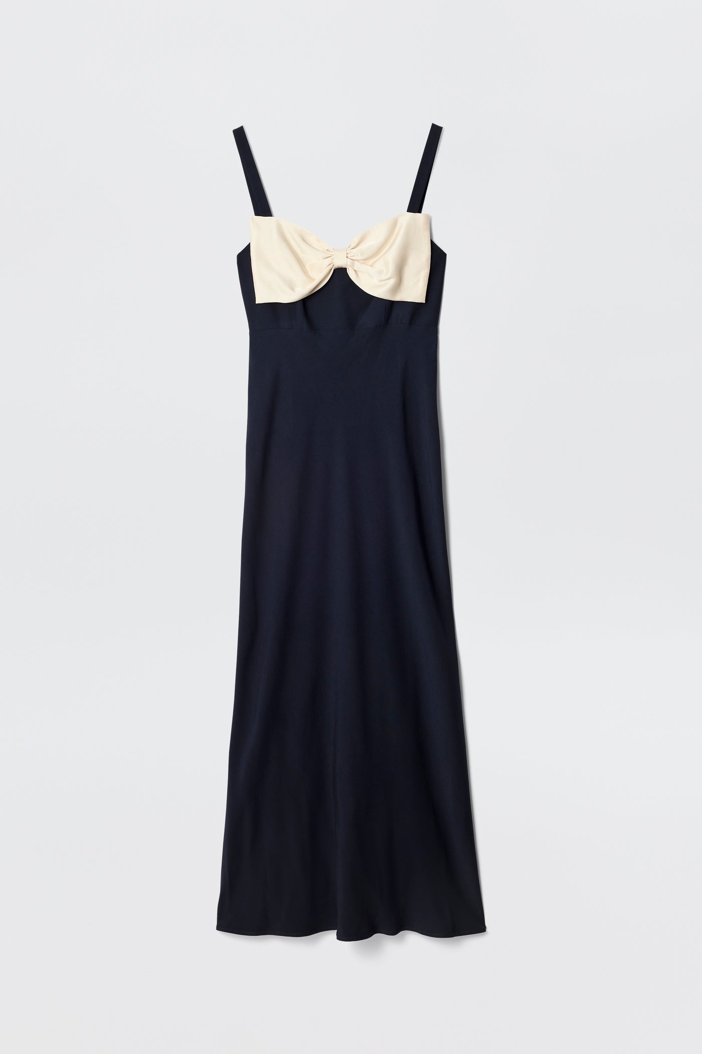 The Melisse is a sleeveless, ankle-length deep navy evening dress with spaghetti straps and a large cream-colored bow at the chest, shown against a plain white background.