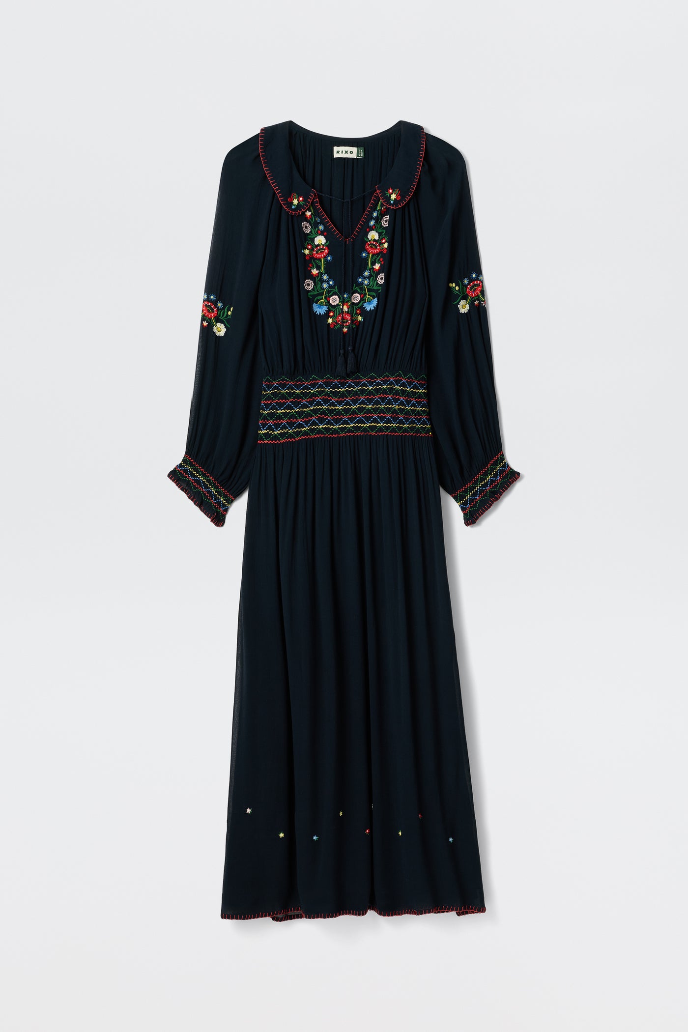 The Emilio - Petunia Embroidery Navy is a long-sleeved navy dress with vibrant floral embroidery on the chest, sleeves, and waistband, featuring a pleated skirt plus decorative stitching along the cuffs and hem.