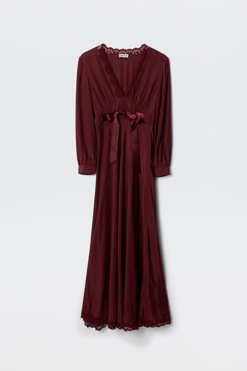 The Adaline – Maroon is a floor-length, long-sleeved maroon dress with lace-trimmed neckline and hem, plus a satin ribbon at the waist, shown against a plain white background.