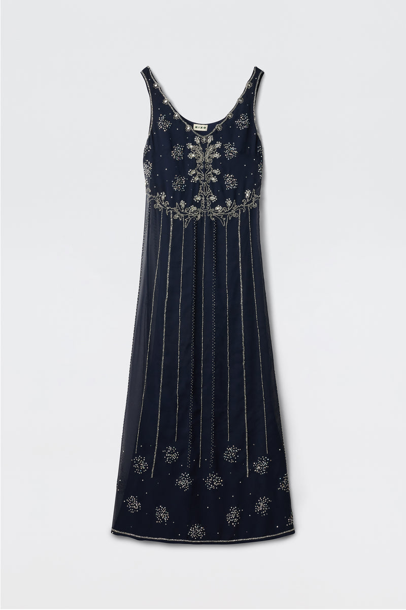 The Silvanna - Tilda Embellishment Navy is a sleeveless, floor-length dress in navy with silver floral embroidery and vertical lines, offering an elegant, classic look. The dress is displayed lying flat on a light background.