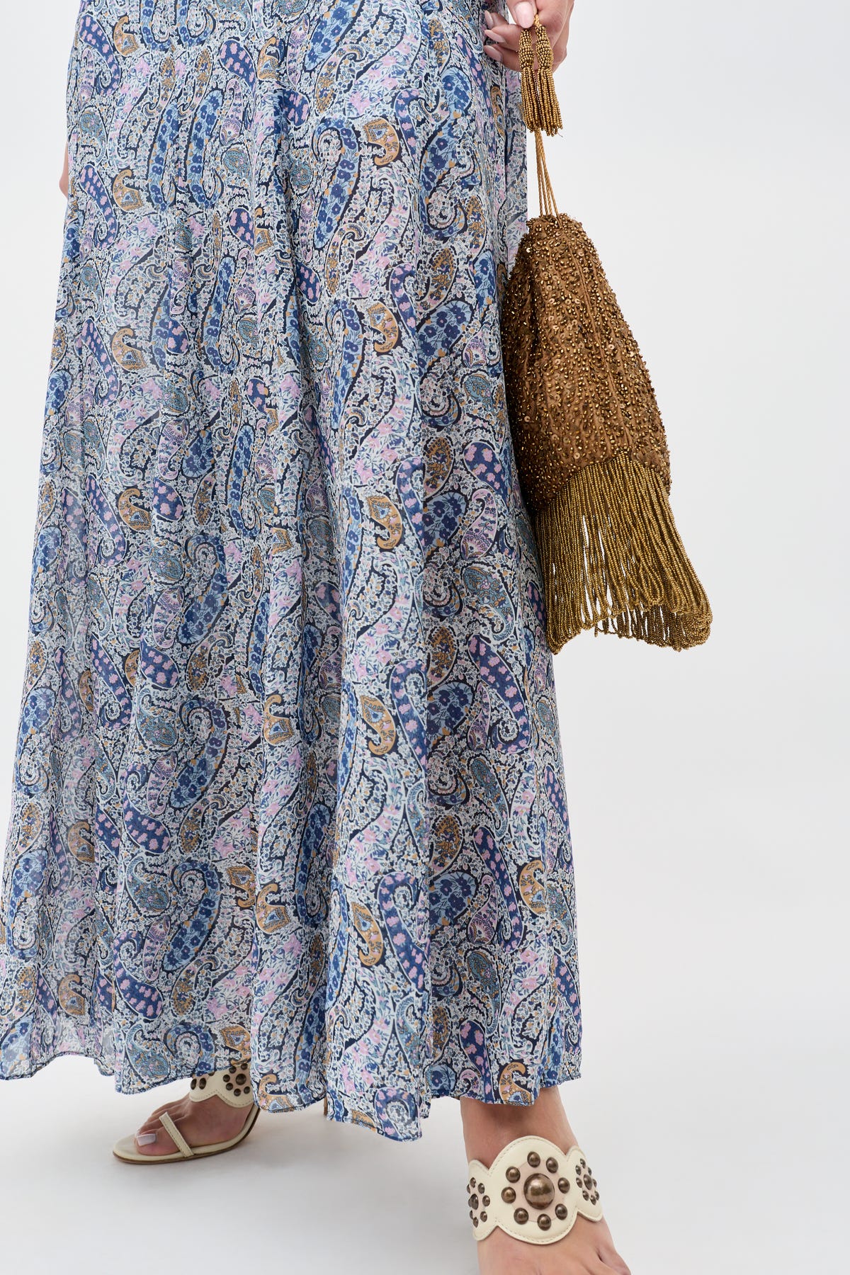 A person showcases the Orla - Vintage Scatter Embellishment Gold skirt, paired with studded white sandals and a brown fringed bag. Only the lower half of the body is visible against a plain background.