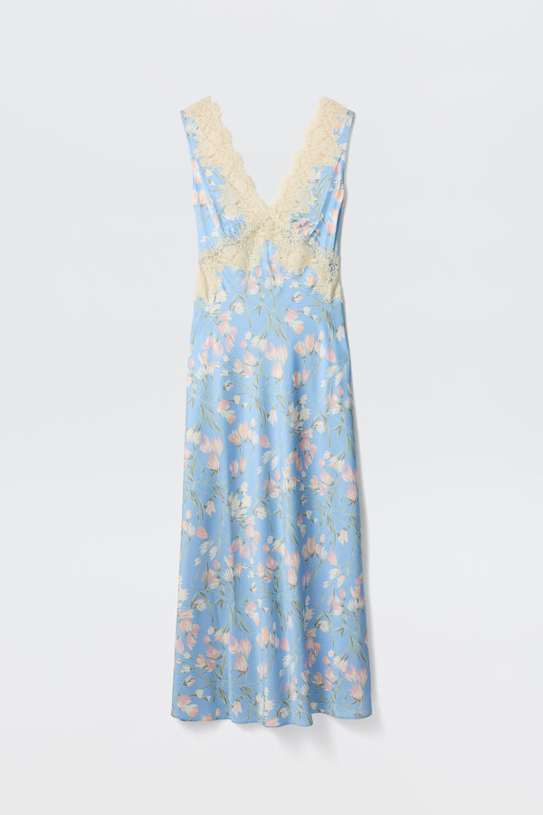 The Lysandra - Watercolour Floral Blue is a long, sleeveless dress featuring a light blue background with pink and white floral print and cream lace trim on the deep V-neck and waist, shown against a plain white backdrop.