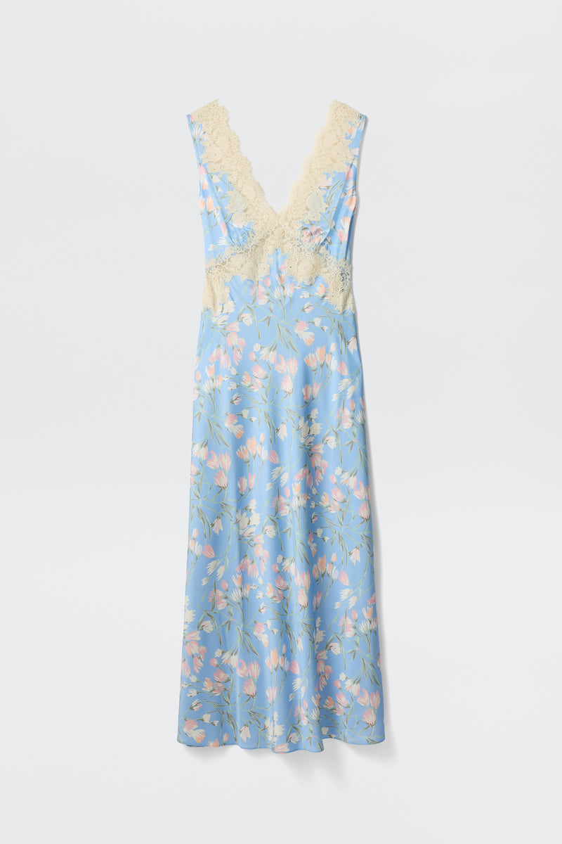 The Lysandra - Watercolour Floral Blue is a long, sleeveless dress featuring a light blue background with pink and white floral print and cream lace trim on the deep V-neck and waist, shown against a plain white backdrop.