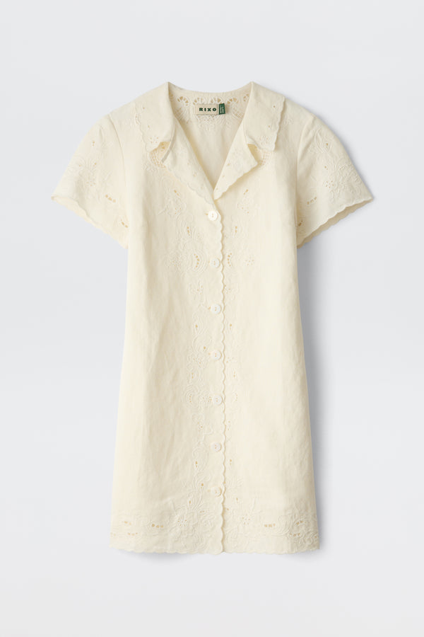 The Zayanna - Esther Cutwork Embroidery Ivory is a short-sleeved, ivory button-up dress featuring a scalloped hem and collar, delicate cutwork embroidery, and crafted from light, airy fabric.