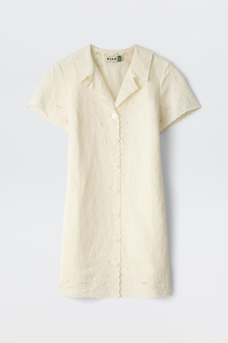The Zayanna - Esther Cutwork Embroidery Ivory is a short-sleeved, ivory button-up dress featuring a scalloped hem and collar, delicate cutwork embroidery, and crafted from light, airy fabric.