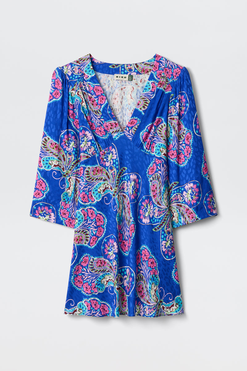 The Margaux - Butterfly Bloom Jacquard Blue dress is a blue V-neck with 3/4 sleeves, a colorful pink, purple, and teal pattern, a subtle sheen, and a relaxed, flowy fit.