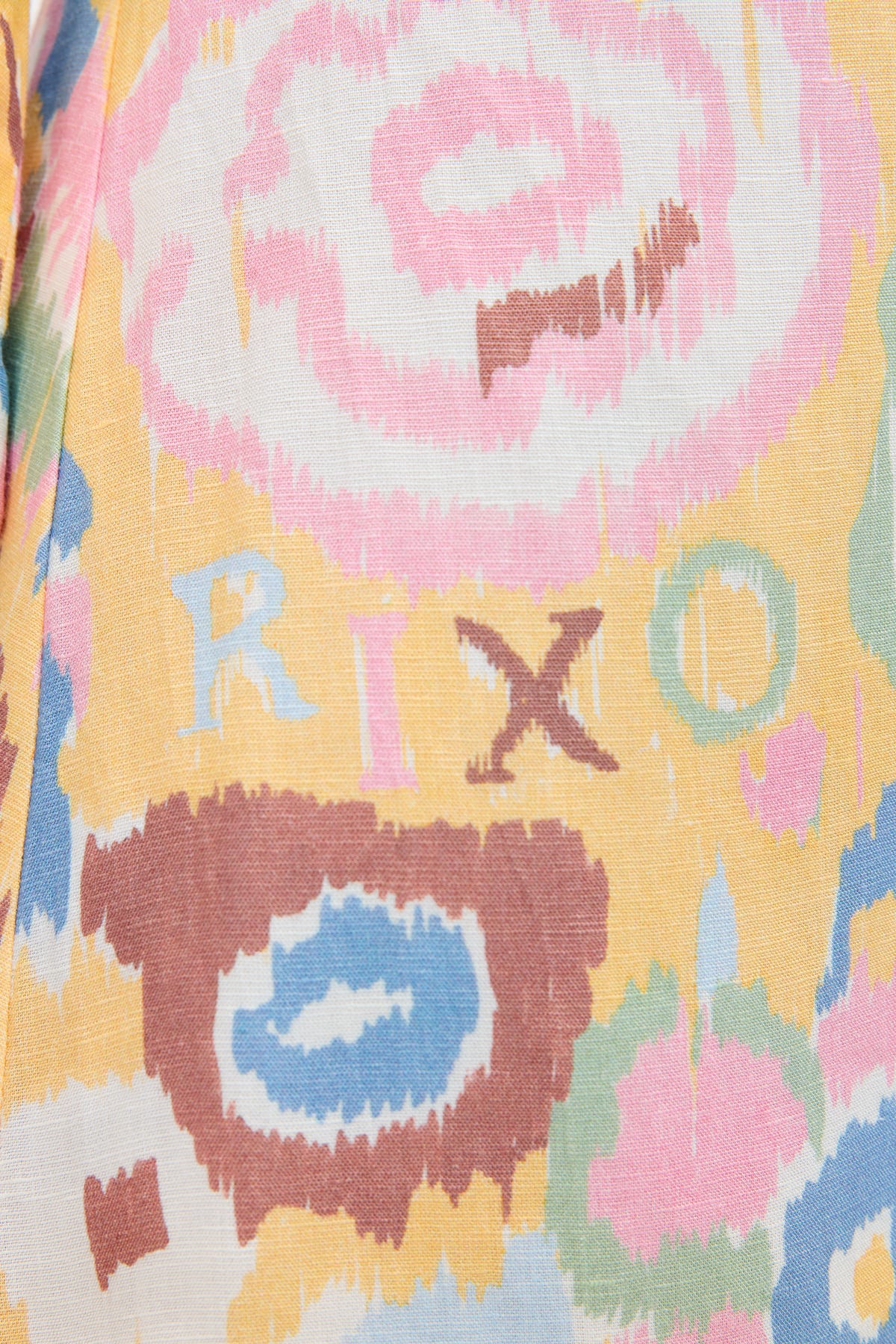 A close-up of Lucien - Ikat Bloom Yellow fabric reveals an abstract pink, yellow, blue, and brown pattern with RIXO lettering—ideal for a vibrant bohemian or linen mini dress.