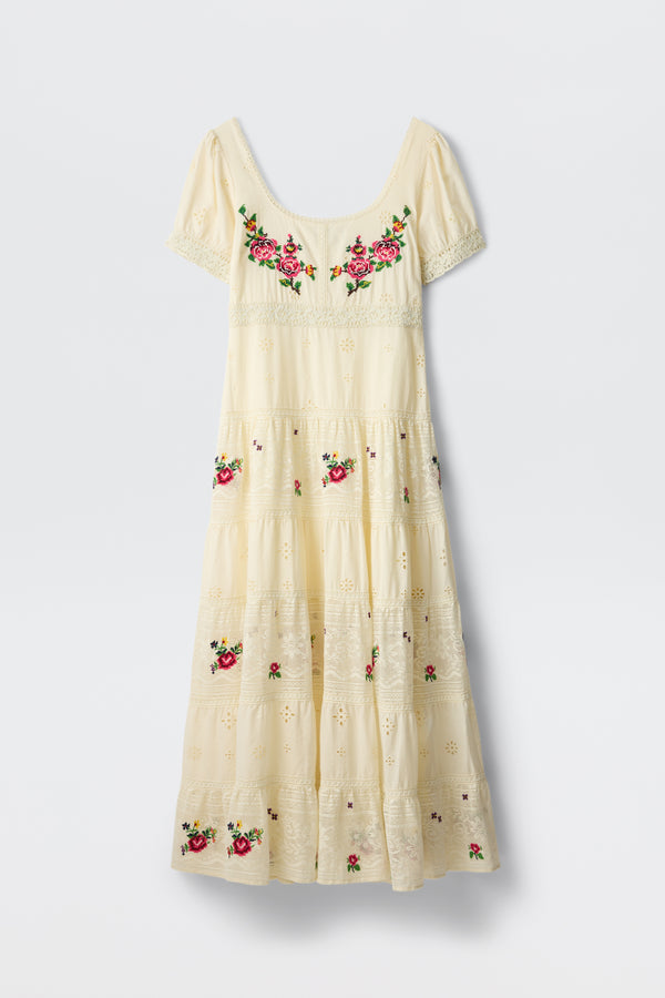 The Cady - Spring Rose Embroidery Cream is a cream-colored, ankle-length dress featuring short sleeves, eyelet details, and vibrant pink rose embroidery on the chest and skirt.