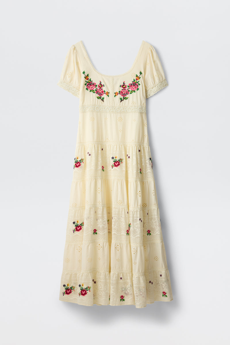 The Cady - Spring Rose Embroidery Cream is a cream-colored, ankle-length dress featuring short sleeves, eyelet details, and vibrant pink rose embroidery on the chest and skirt.