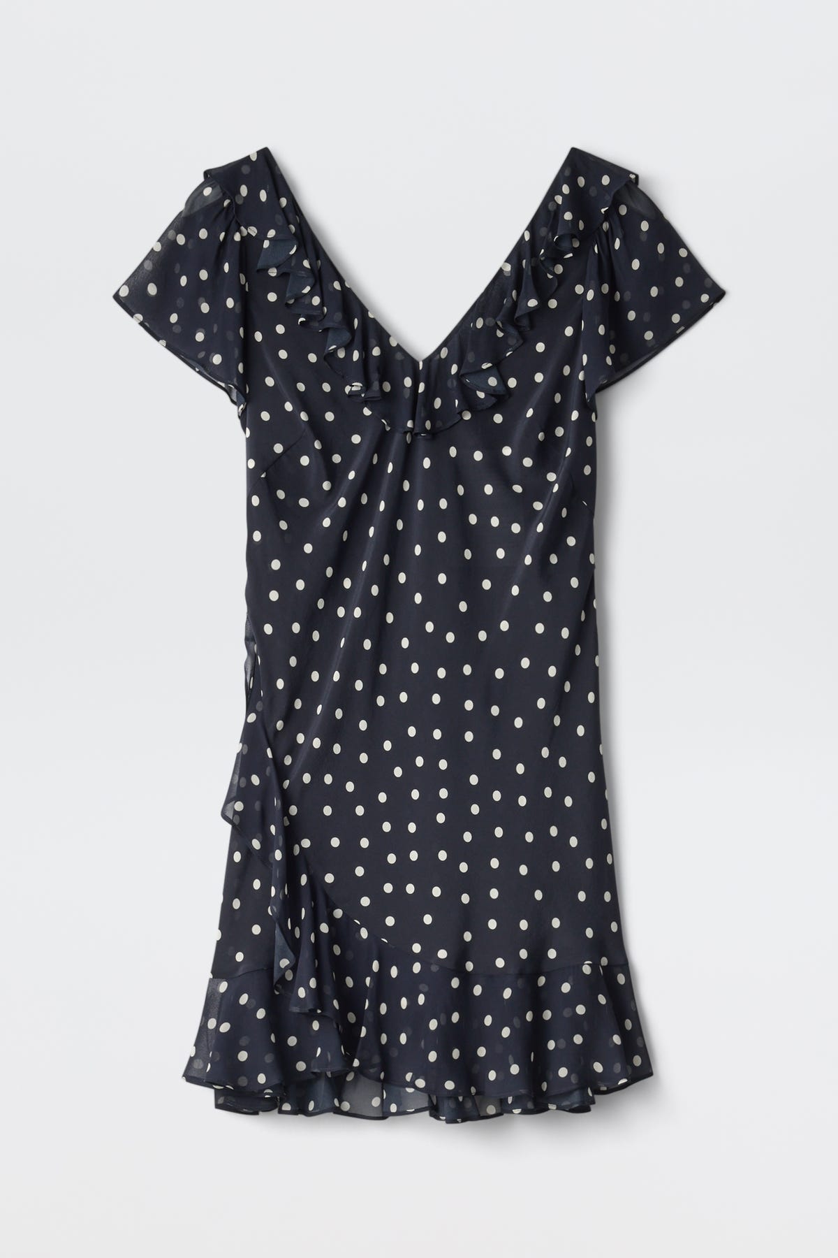 The Tally - Layla Dot Navy is a short-sleeved, navy blue dress with white polka dots, a V-neckline, ruffle details on the neckline and hem, and a slightly flared above-the-knee skirt.