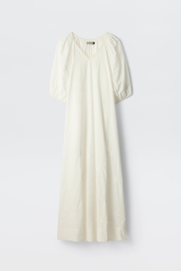 The Gizele - Daisy Floral Embroidery White is a long, white dress featuring short puff sleeves, a V-neckline, and delicate daisy floral embroidery details, displayed against a plain white background.