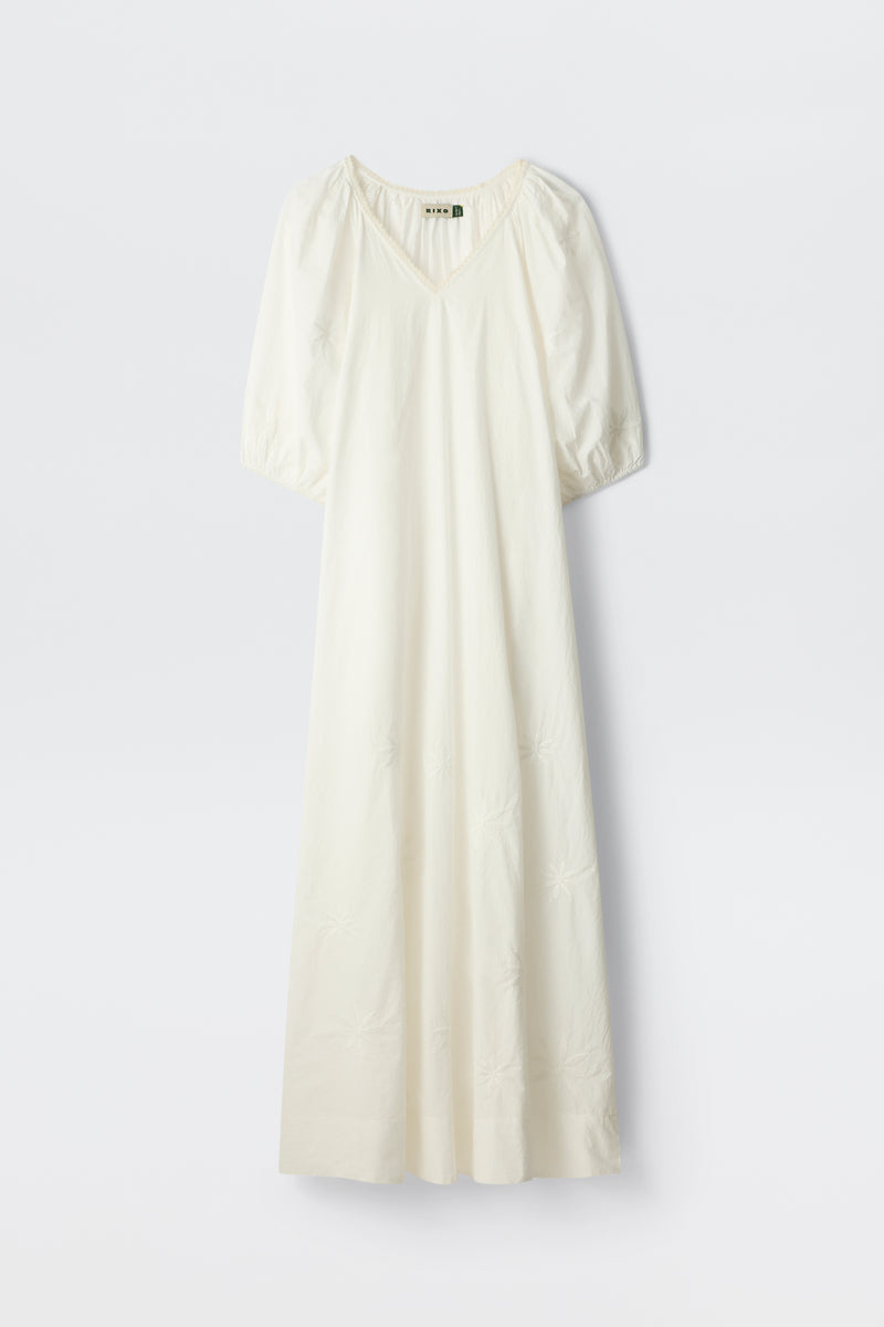 The Gizele - Daisy Floral Embroidery White is a long, white dress featuring short puff sleeves, a V-neckline, and delicate daisy floral embroidery details, displayed against a plain white background.