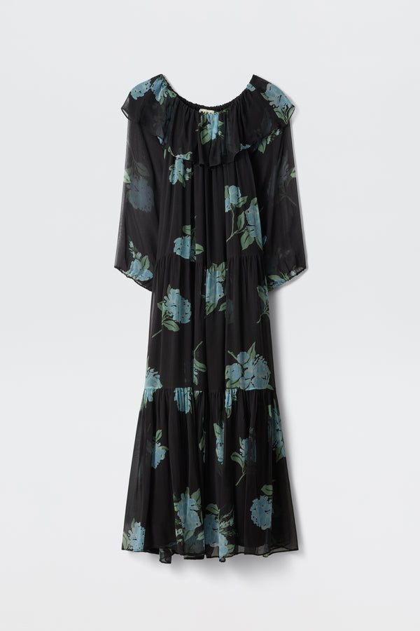 A long-sleeved, ruffled maxi dress in charcoal, featuring blue peony scatter prints and a ruffled off-the-shoulder neckline, is displayed against a plain white background. This dress is named "Lela - Peonies Scatter Charcoal.