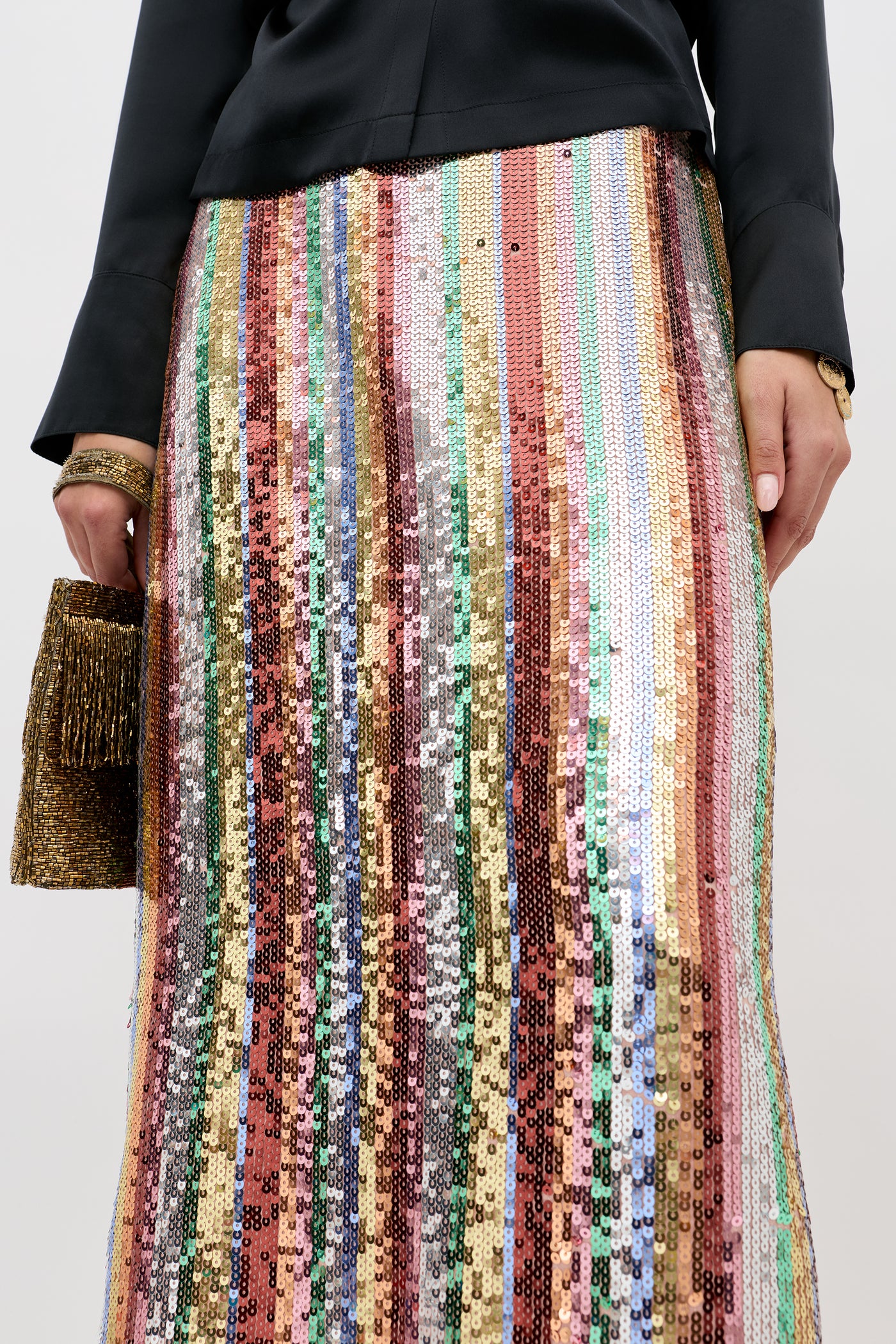 A person wearing the Kelly Dixie Stripe Embellishment Multi skirt, a black long-sleeved top, and holding a gold fringed clutch.