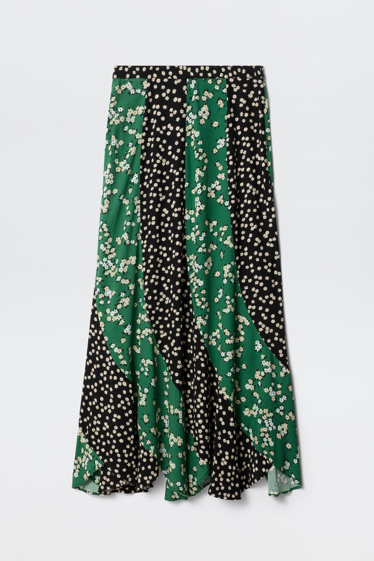 The Gracella - City Floral Mix Olive is a long, flowy midi skirt with alternating black and green panels in a small white floral print. It features a mid-rise waist, slightly flared hem, and is perfect for transitional dressing.