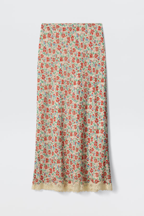 The Stassie - Jeannie Bloom Ivory is a long, straight skirt featuring a colorful red, green, and blue floral pattern on an ivory base with delicate beige lace trim along the hem.