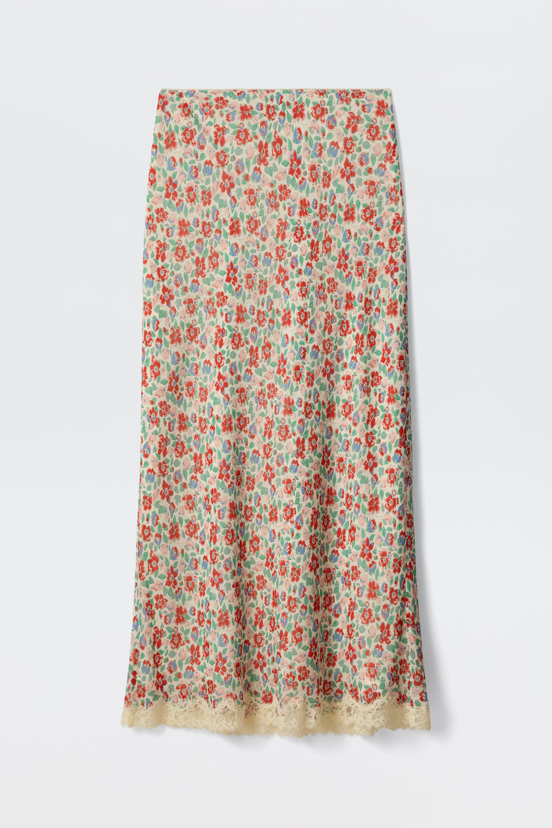 The Stassie - Jeannie Bloom Ivory is a long, straight skirt featuring a colorful red, green, and blue floral pattern on an ivory base with delicate beige lace trim along the hem.
