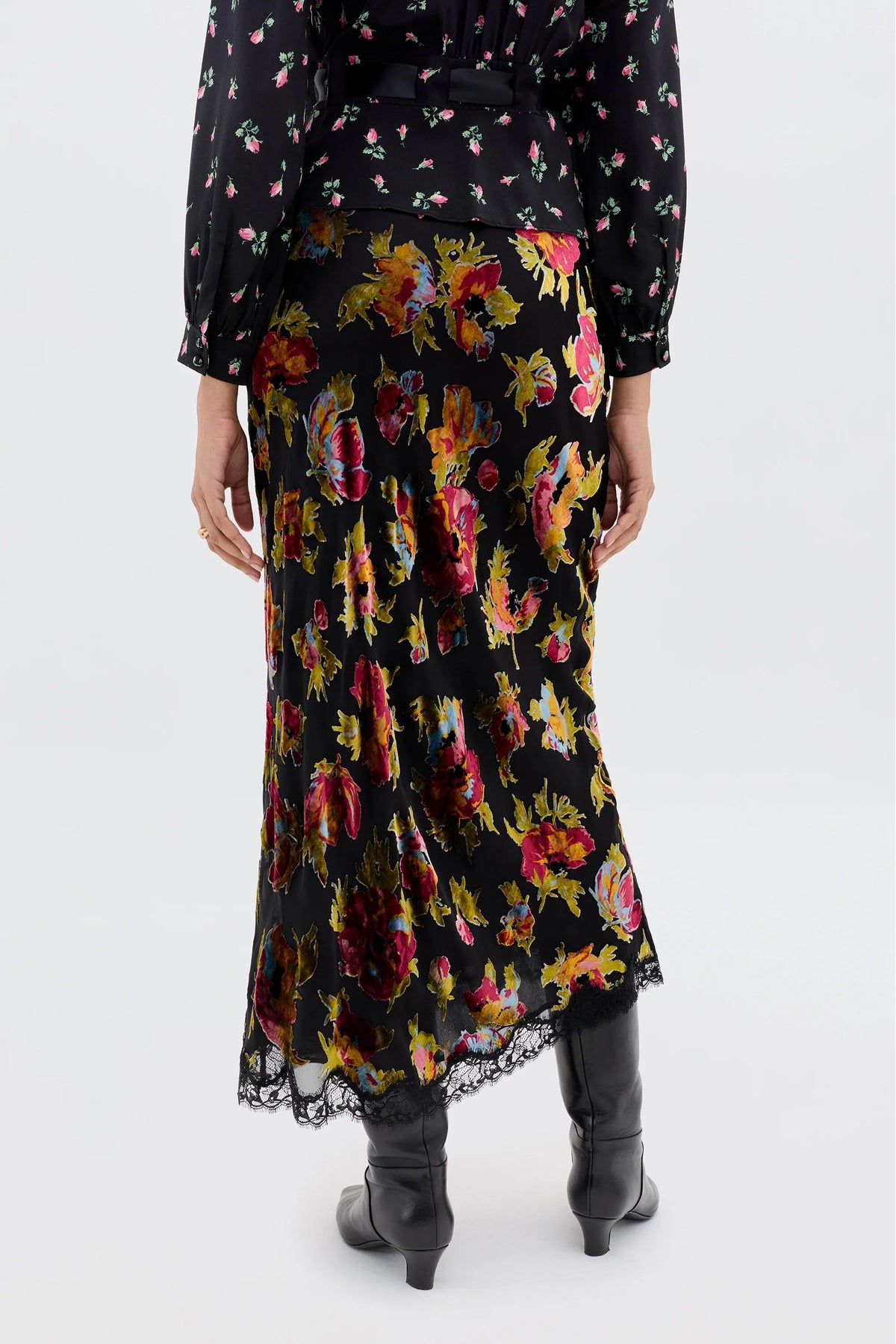 Someone is shown from the back wearing the Stassie - Countryside Devoré Black blouse with a romantic black floral skirt featuring lace trim, paired with black boots, set against a plain background.