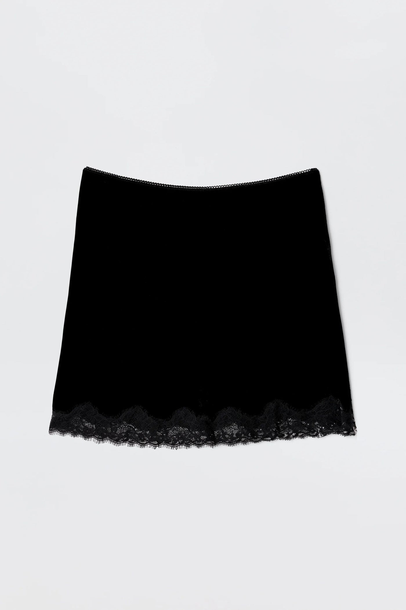 The Kornelia - Black is a nineties-inspired black velvet mini skirt with a straight fit and delicate lace trim at the hem, shown against a plain light background.
