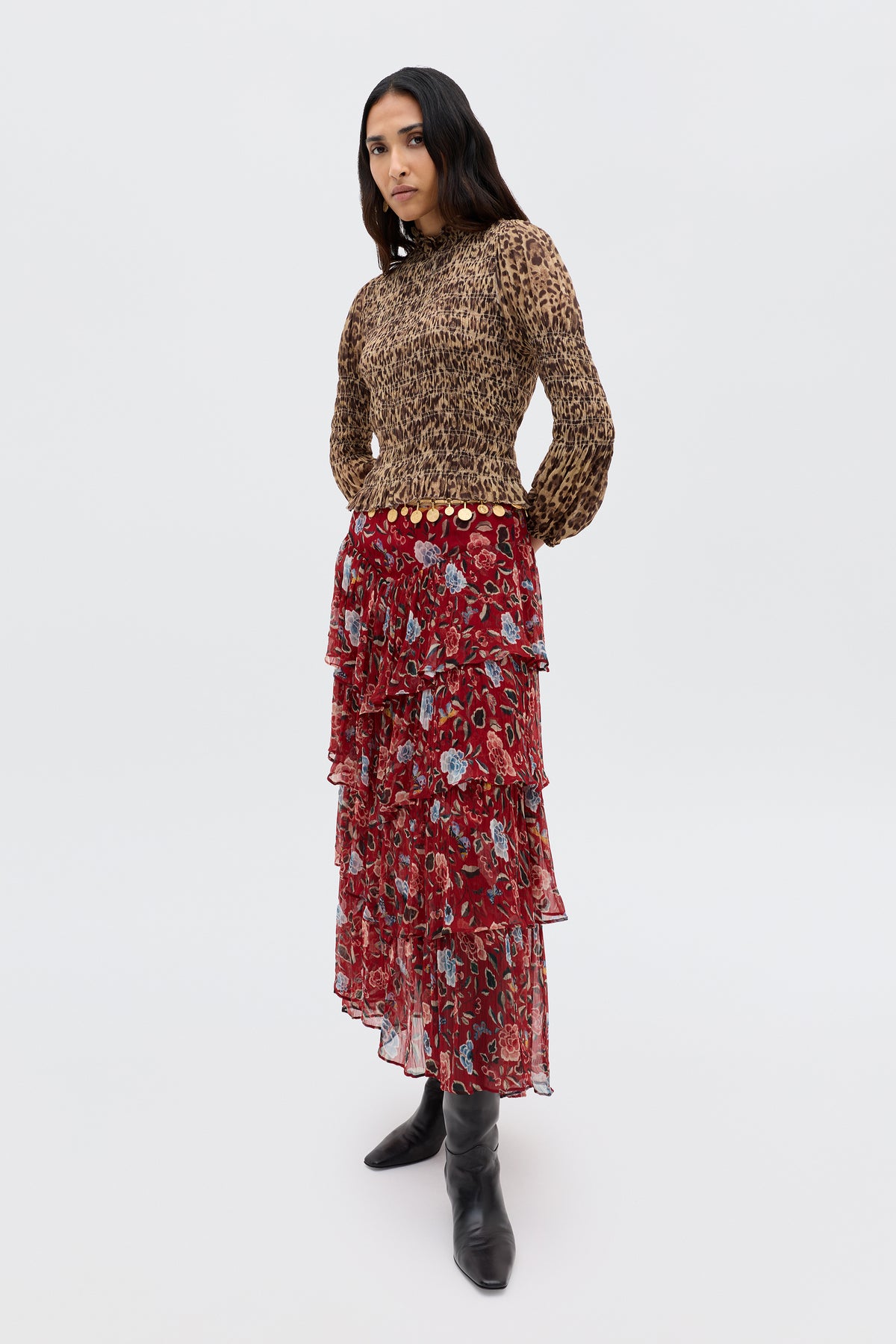 A woman stands confidently against a plain background, wearing the Taryn - Butterfly Floral Burgundy tiered prairie skirt with a leopard print long-sleeve top and black boots, her hands behind her back as she looks at the camera.