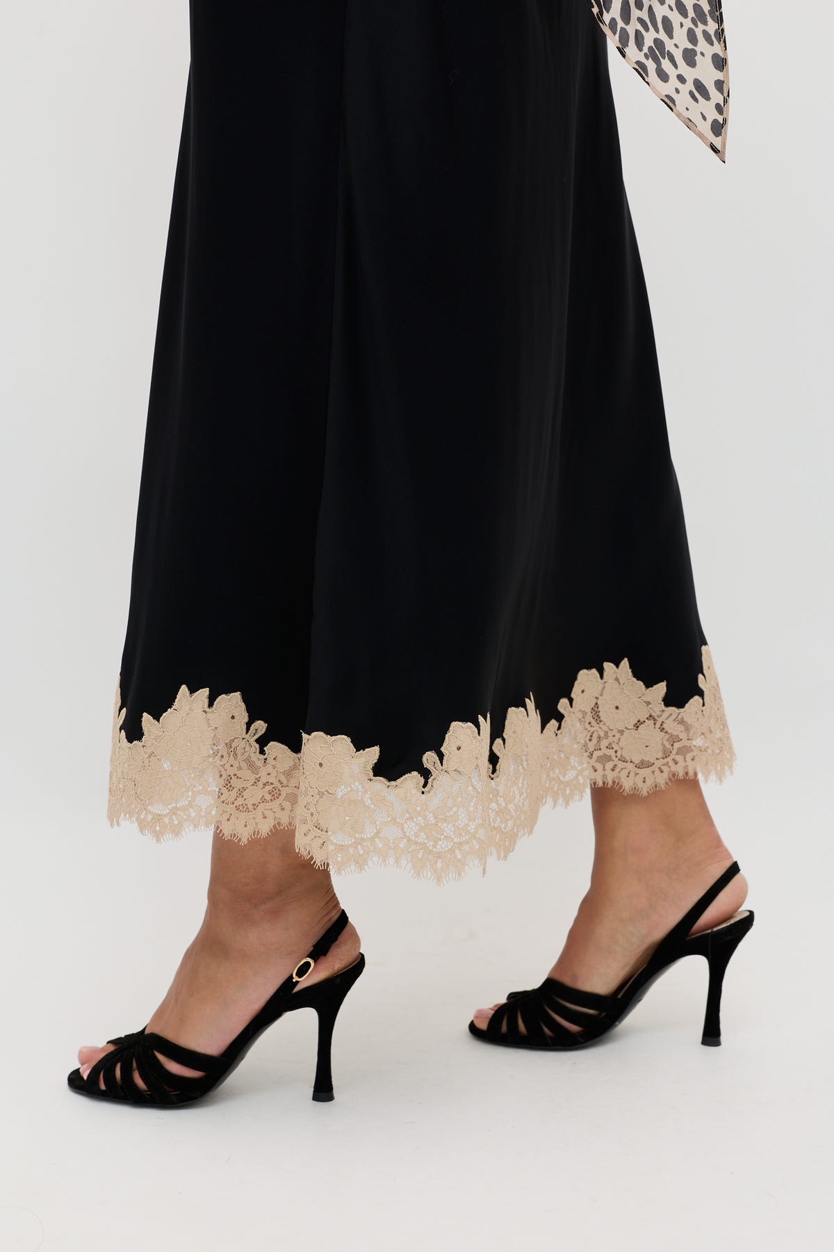A person wearing the Matilde - Black long skirt with beige lace trim at the hem and black high-heeled sandals, standing on a white background.
