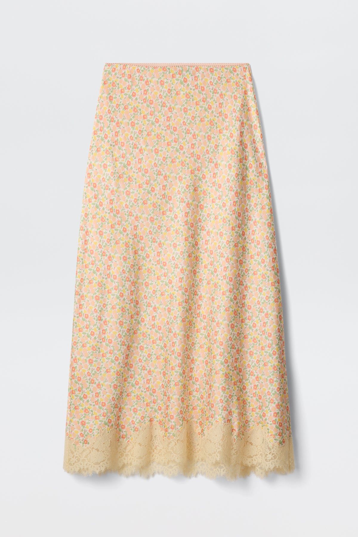 The Matilde - Katie Floral Cream is a long slip skirt in pastel yellow, featuring a colorful floral print and scalloped lace hem, shown on a plain white background.