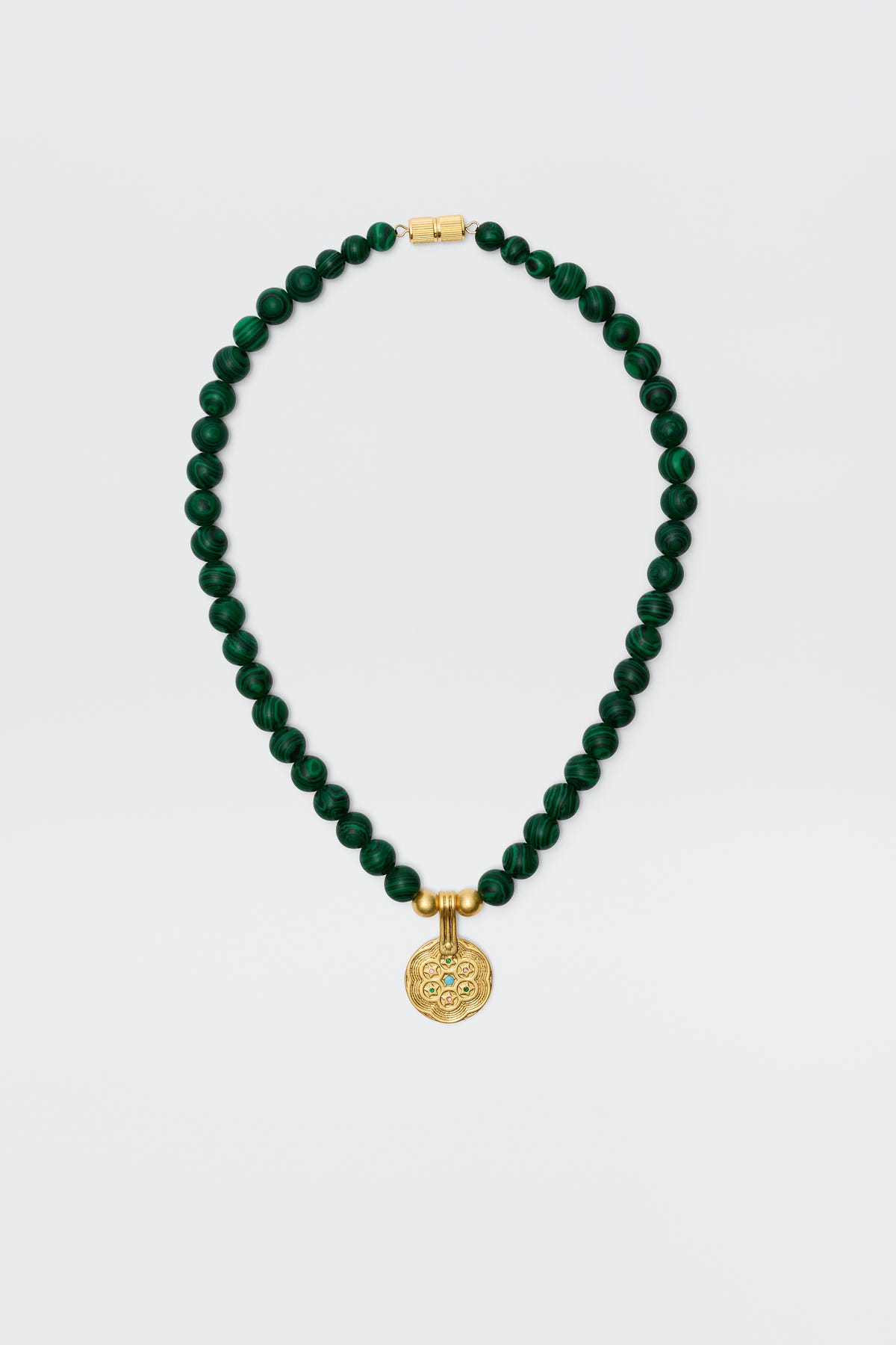 The Ischia - Green necklace features round dark green malachite beads with a gold clasp and an engraved golden pendant, displayed on a plain white background.