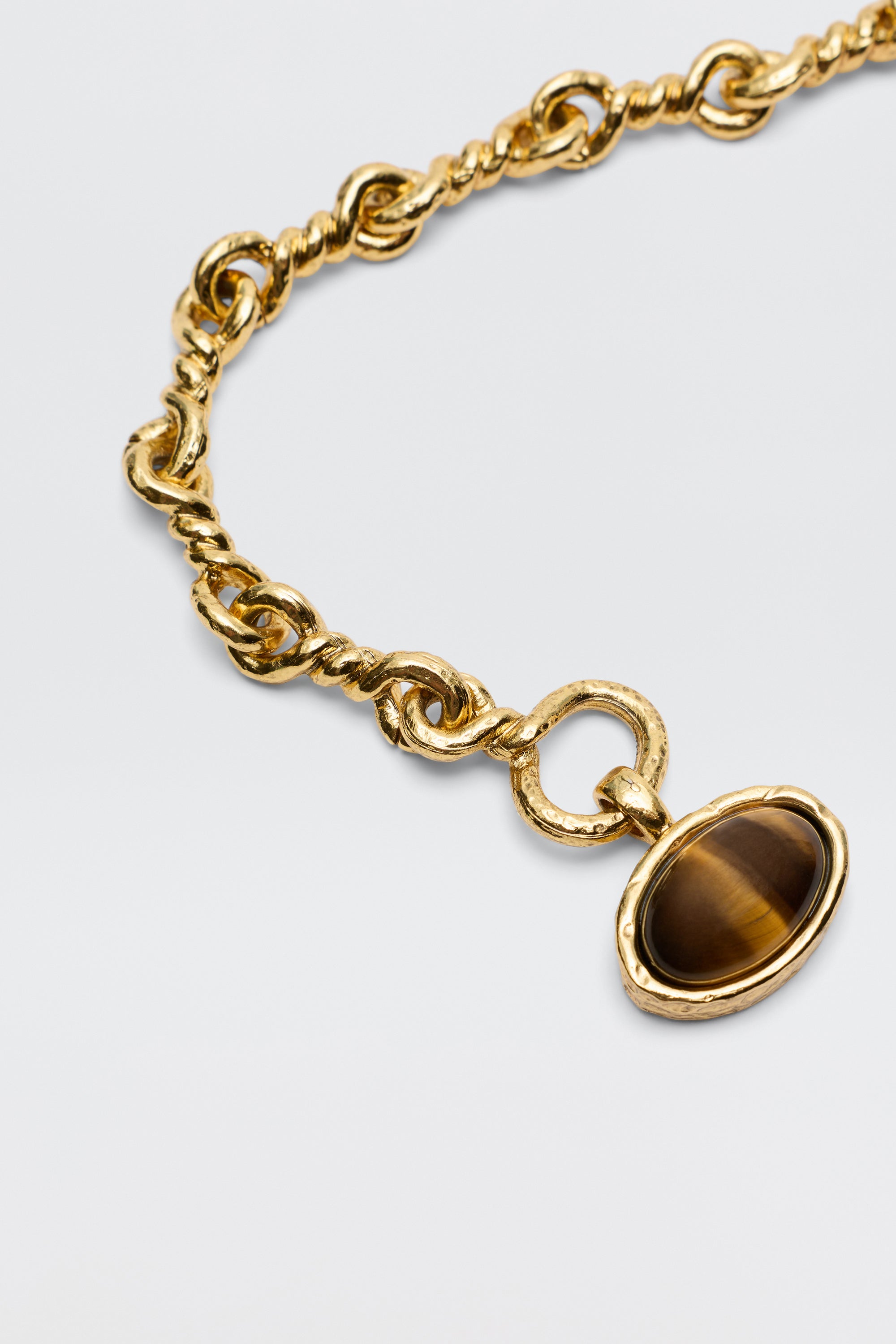 The Zandra - Gold necklace features a chunky, vintage-inspired gold-plated chain with twisted links and a round pendant set with an oval brown gemstone, shown on a light background.