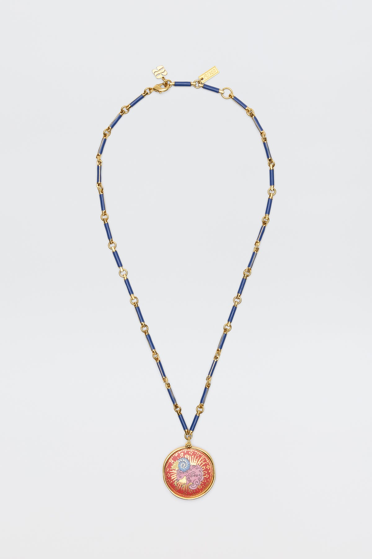 The Ari - Astro Aries necklace features a gold and blue chain with a circular red and gold sunburst pendant, displayed on a plain white background.