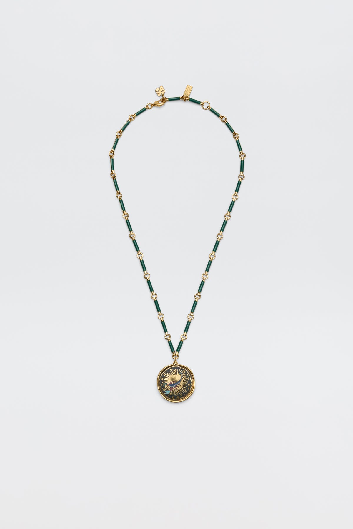 The Ari - Astro Scorpio necklace features gold and green beads with an ornate round pendant bearing an embossed design, displayed elegantly on a plain white background.