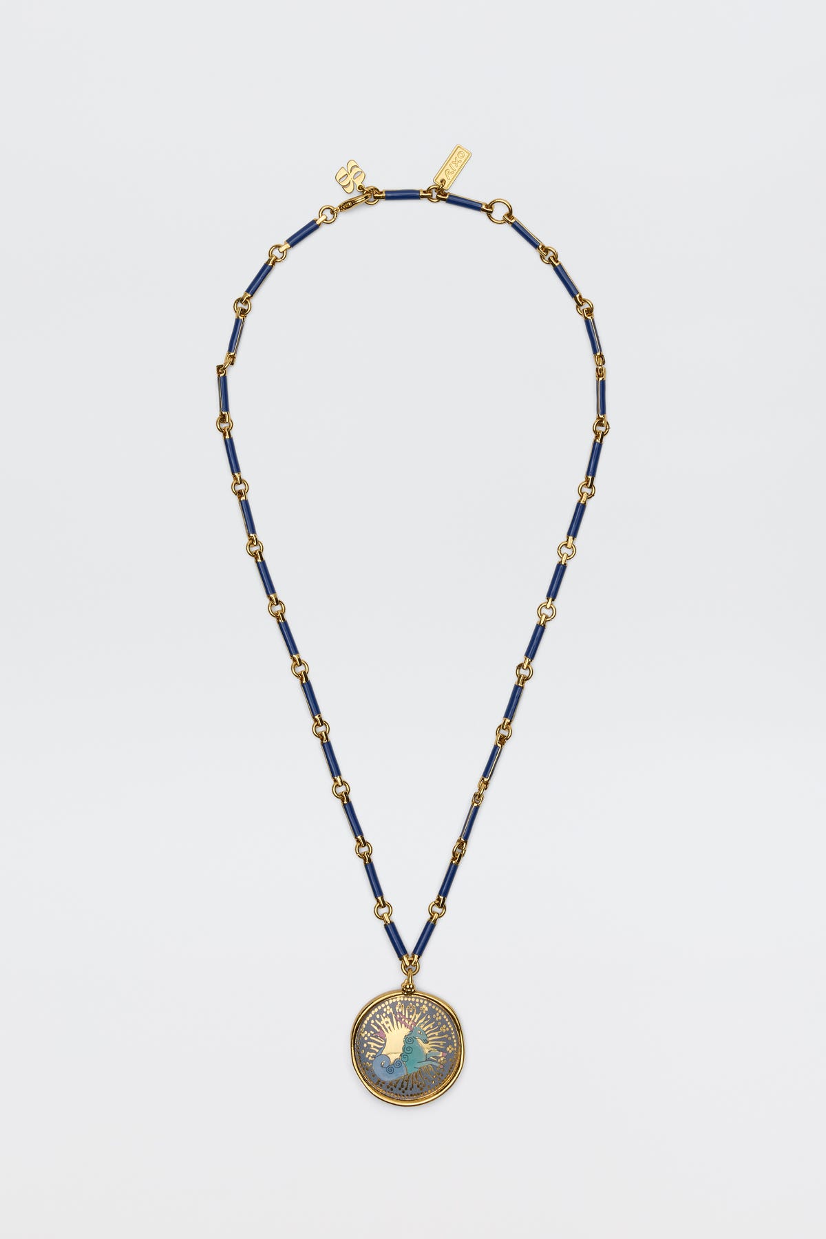 The Ari - Astro Capricorn necklace features gold and navy blue beads with a statement disc charm of a woman’s profile and radiating rays, shown against a plain white background.