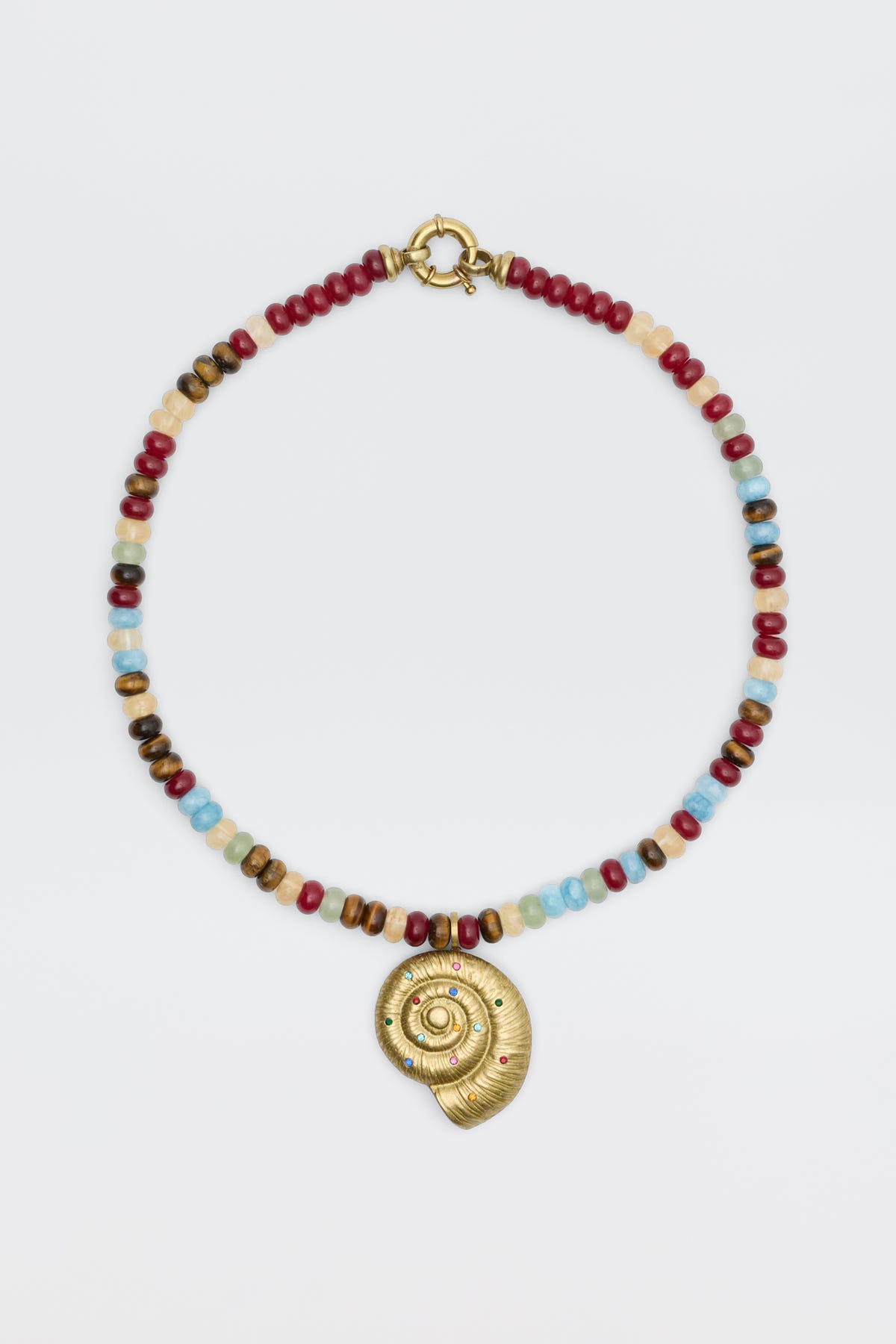 The Parma - Multi beaded necklace showcases red, blue, brown, and white beads with a gold spiral shell pendant adorned with small colored gemstones, elegantly displayed on a white background.