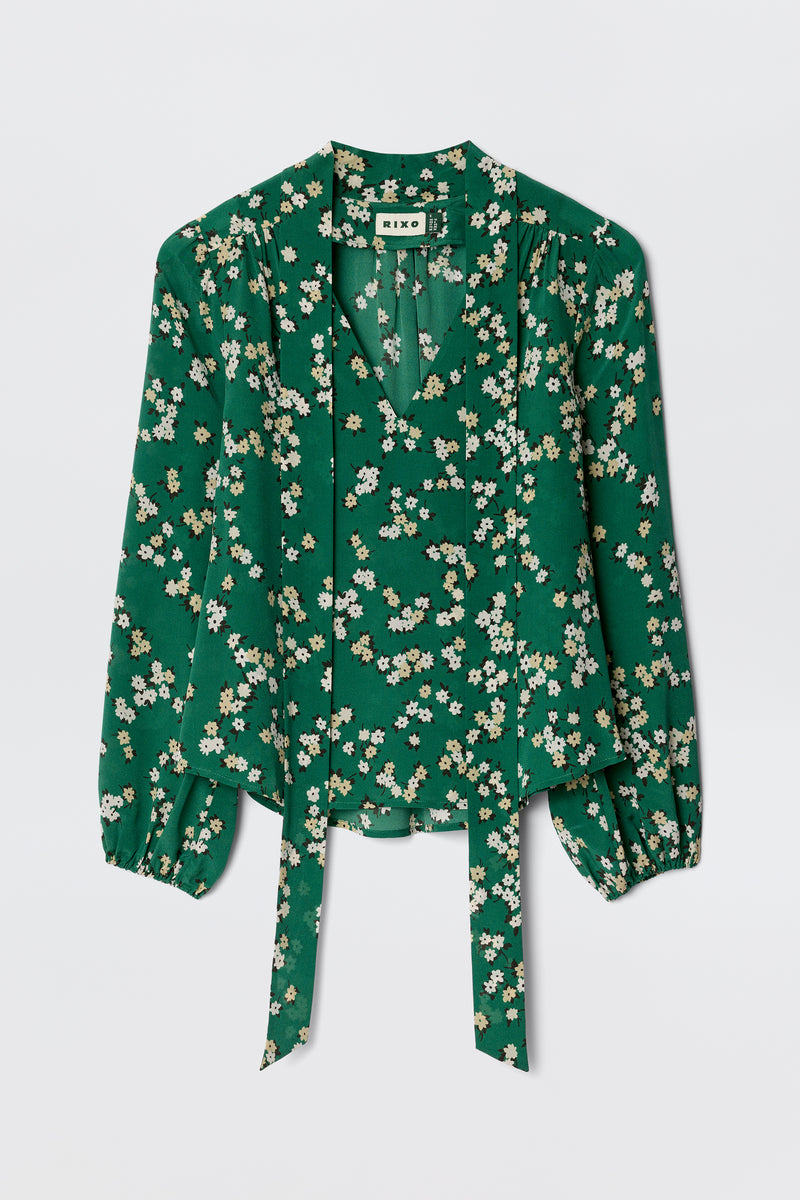 The Moss - City Floral Olive is a vintage-inspired green silk blouse with white and yellow florals, a v-neck, gathered shoulders, and two long front ties.
