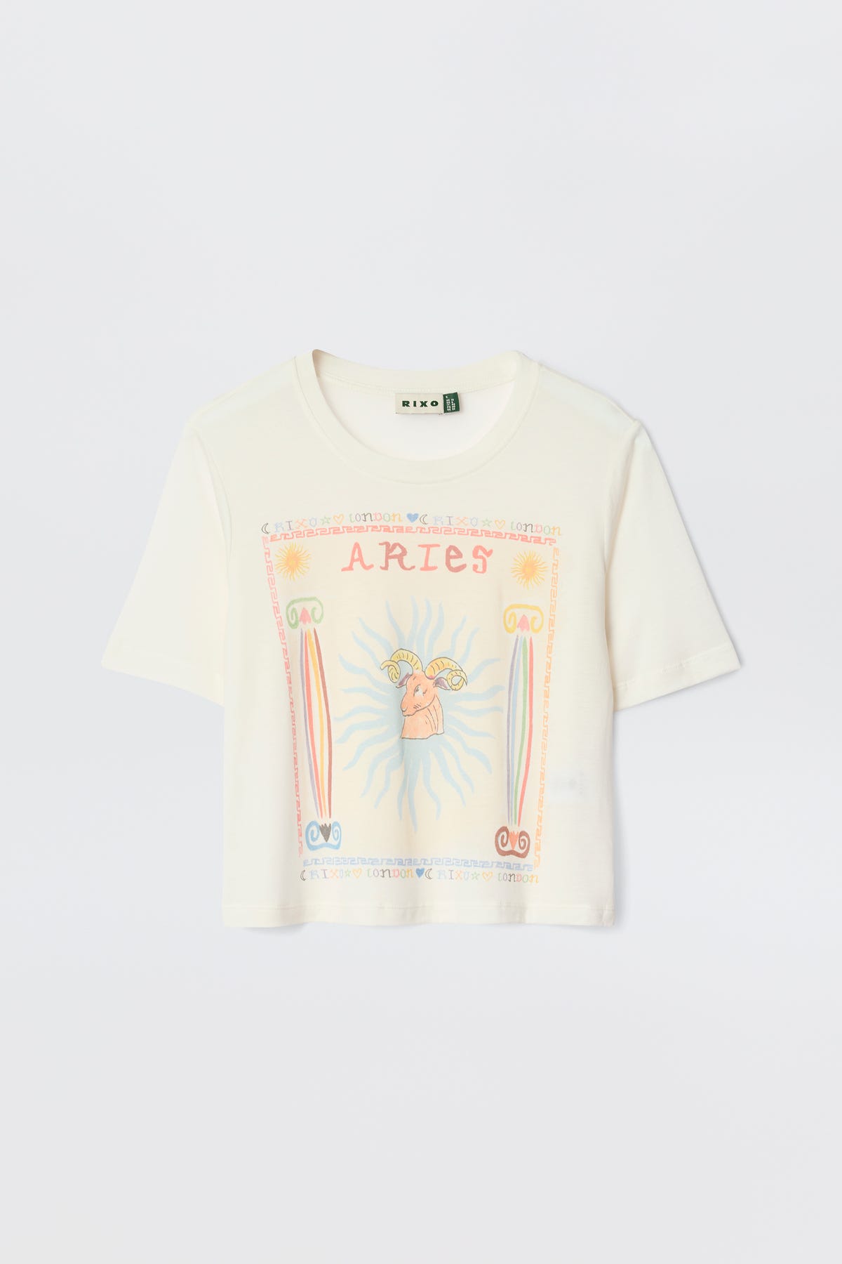 The Ria - Aries white short-sleeve T-shirt displays a vibrant Aries graphic with "ARIES" at the top, a central ram, sun rays, and pink, orange, and blue astrological symbols.