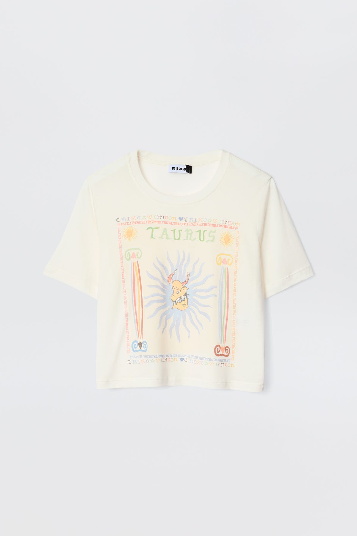 The Ria - Taurus is a cream short-sleeve tee with a vibrant Taurus illustration, astrological symbols, sun rays, and pastel decorative borders—ideal for pairing with RIXO skirts.