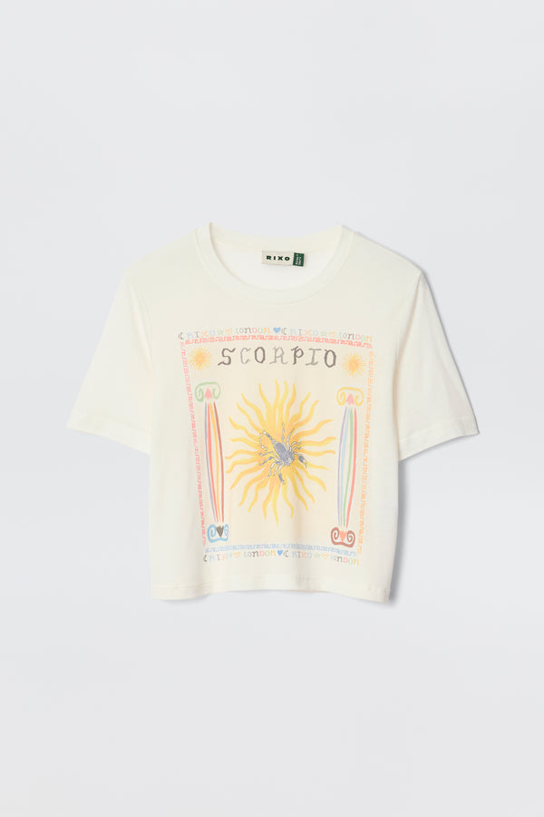The Ria - Scorpio is a white cropped T-shirt with a vibrant Scorpio illustration—sun, scorpion, and zodiac symbols—designed to pair perfectly with RIXO skirts. Laid flat on a plain background for an eye-catching astrological statement.