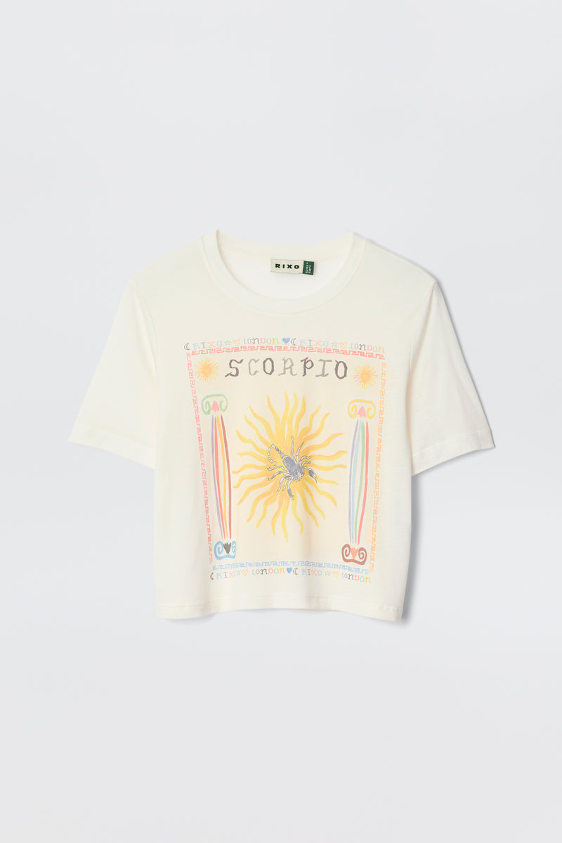 The Ria - Scorpio is a white cropped T-shirt with a vibrant Scorpio illustration—sun, scorpion, and zodiac symbols—designed to pair perfectly with RIXO skirts. Laid flat on a plain background for an eye-catching astrological statement.