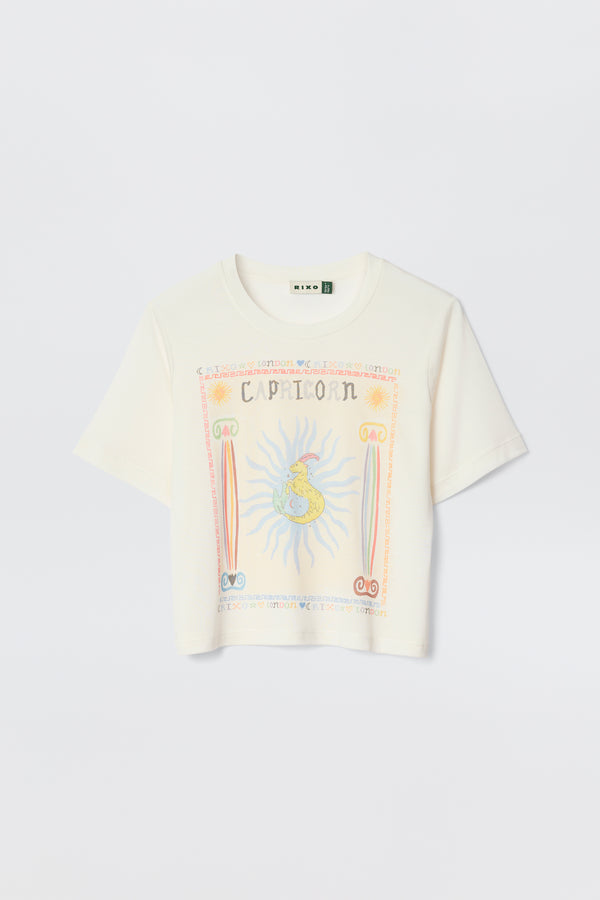 The Ria - Capricorn white short-sleeve T-shirt showcases a bold Capricorn graphic with a sun, astrological symbols, and decorative borders on the front. Ideal with RIXO skirts, it's photographed on a plain light background.