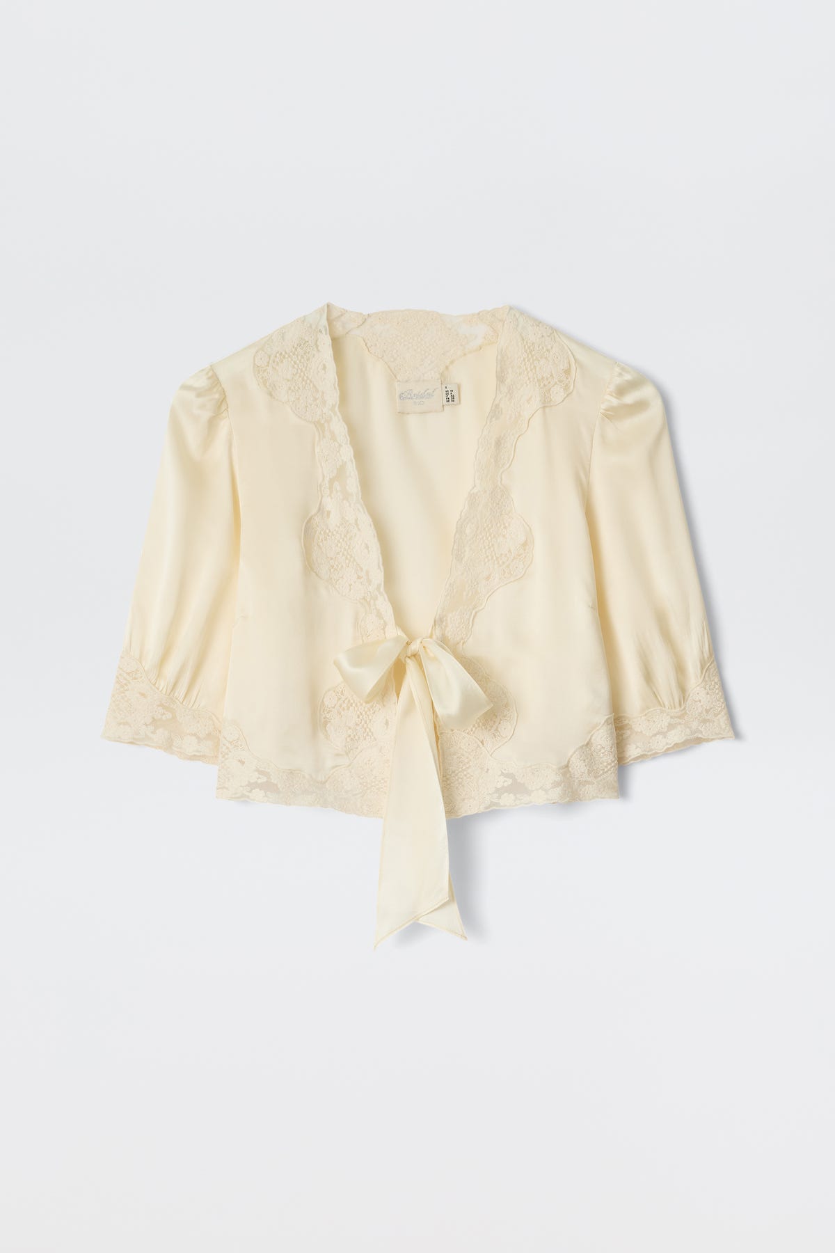 The Amara - Champagne is a light cream satin blouse with delicate lace trim, three-quarter sleeves, and a deep V-neckline that ties at the front—ideal for bridal looks or any elegant occasion.
