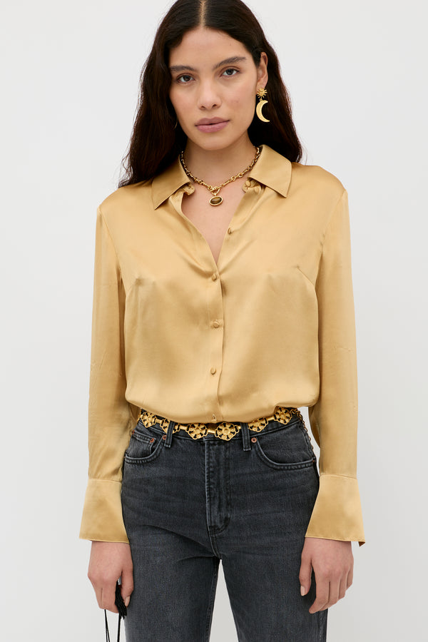 A woman with long dark hair wears the Havan - Gold button-up blouse with dark high-waisted jeans, gold accessories, and stands against a plain white background.