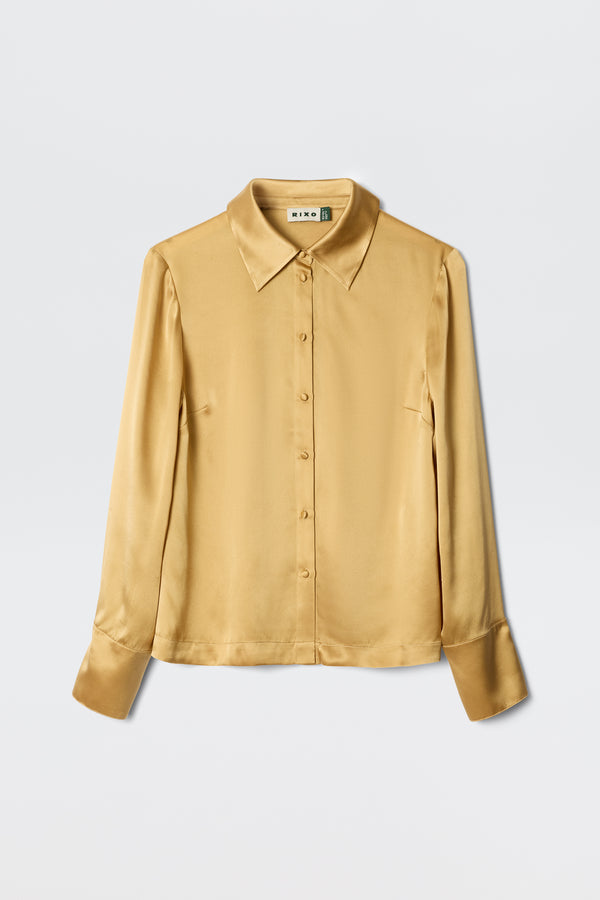 The Havan - Gold is a long-sleeved satin button-up blouse with a pointed collar and wide cuffs, shown against a plain white background.