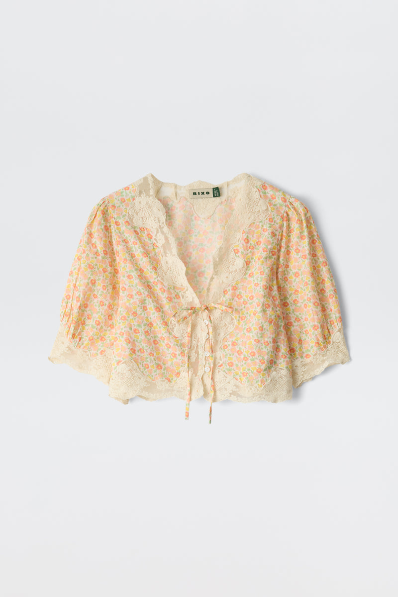 The Ursula - Katie Floral Cream is a vintage-inspired cotton top with a floral print, cropped fit, scalloped lace edges, and a tie-front closure, displayed on a plain white background.