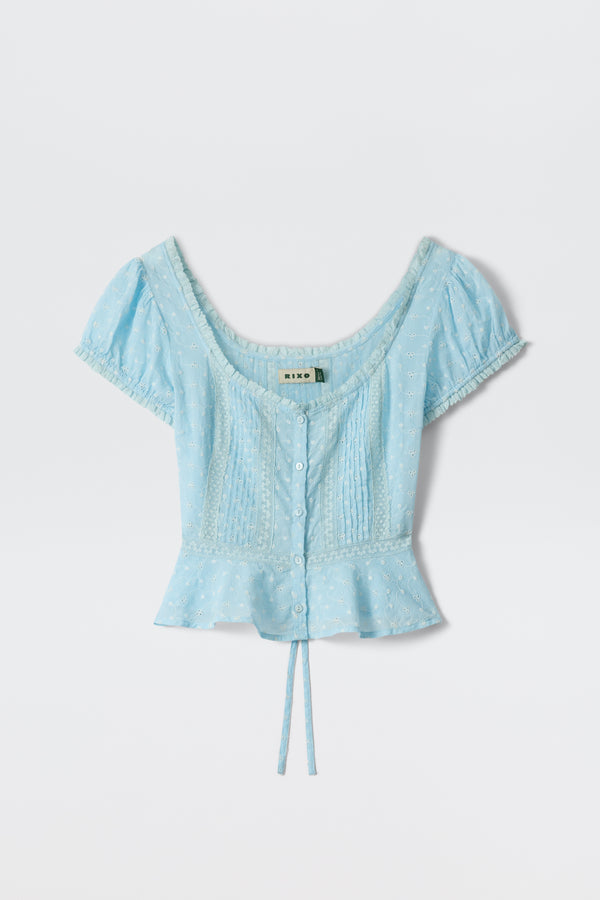 Sandi - Powder Blue: a short-sleeve top with a scoop neckline, button-down front, pintuck details, broderie anglaise-style floral embroidery, peplum hem, and tie waist—shown on a plain white background.
