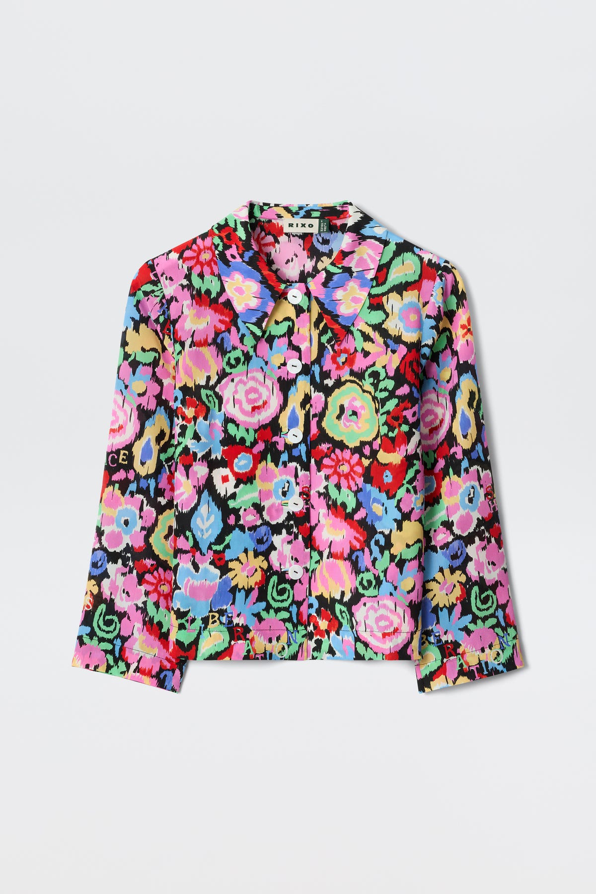 The Ginette - Ikat Bloom Charcoal is a long-sleeve, collared jacket with a vibrant, multicolored floral pattern in pink, blue, green, yellow, and red on a black background, shown against a white surface.