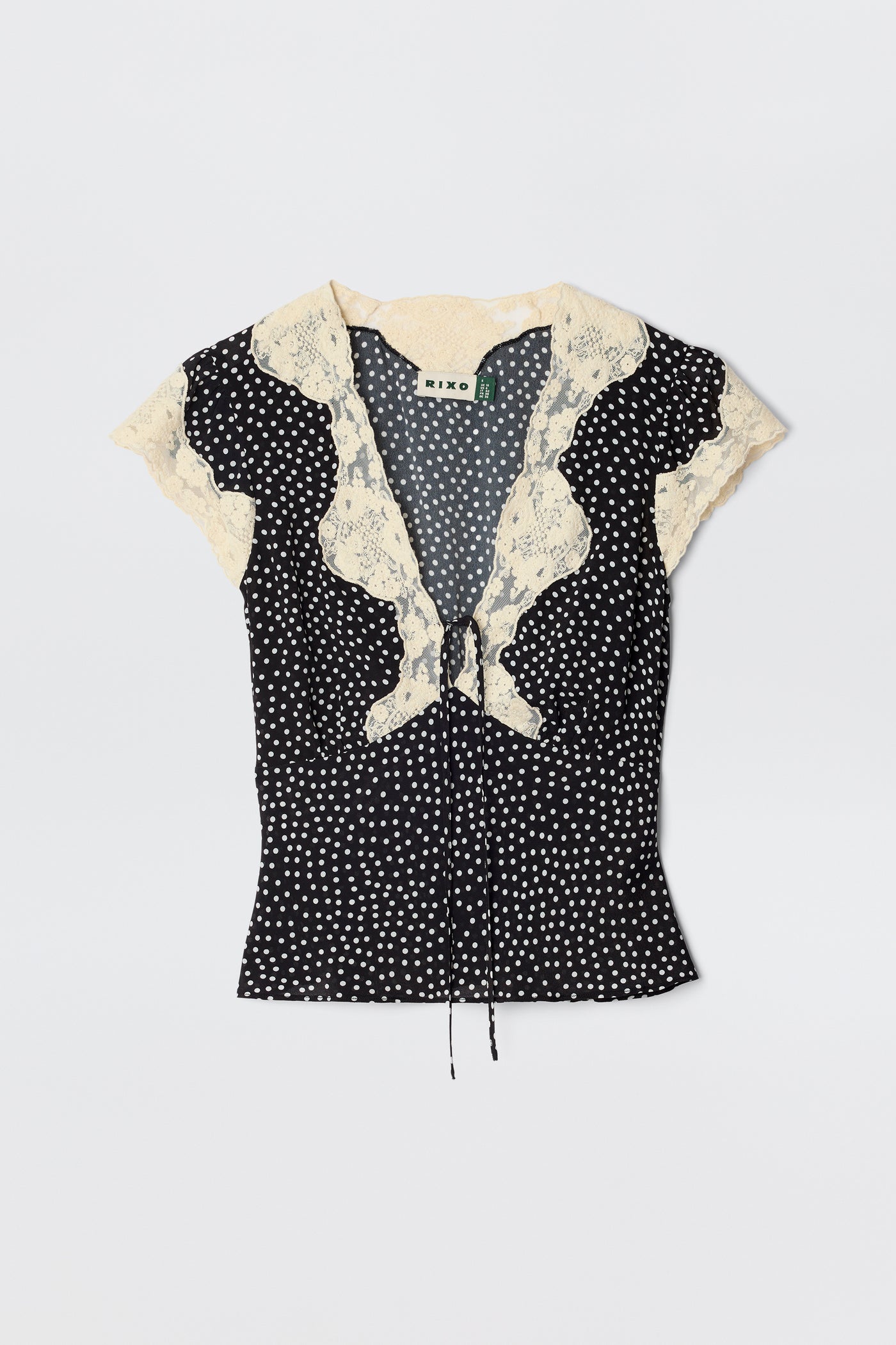 The Elaine - Mini Polka Dot Black is a vintage-inspired, short-sleeved blouse with white polka dots, a cream lace collar, front ruffle, neckline tie, and a fitted silhouette.