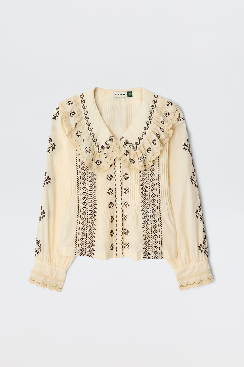 The Percy Mila Embroidery Brown is a cream long-sleeve blouse with brown embroidery, scalloped ruffled collar and cuffs, offering a vintage-inspired, delicate, and feminine look.