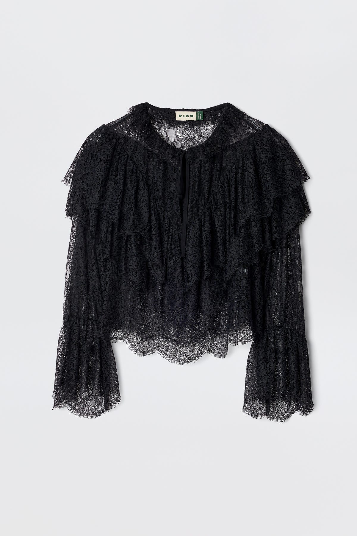 The Faryn - Black is a long-sleeve lace blouse featuring layered ruffles on the chest and sleeves with scalloped hem and cuffs, shown on a plain white background.