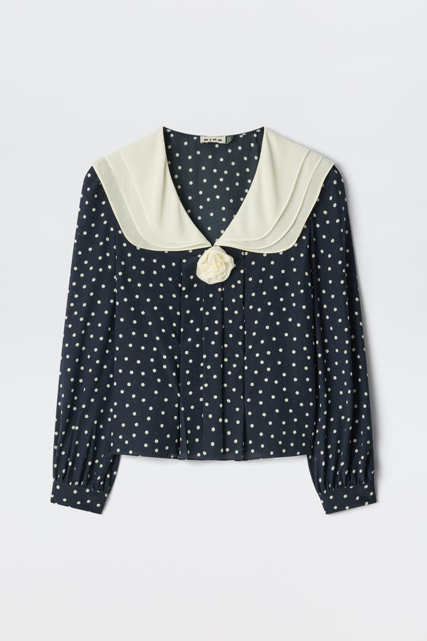 The Emelin Layla Dot Navy is a navy blue blouse with white polka dots, long sleeves, a wide cream sailor collar, and a decorative cream fabric flower at the front.