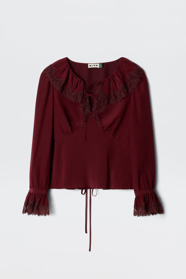 The Aimme - Maroon blouse features long sleeves, lace-trimmed ruffled neckline and cuffs, a tie at the neck, and a drawstring cinched waist, shown against a plain light background.